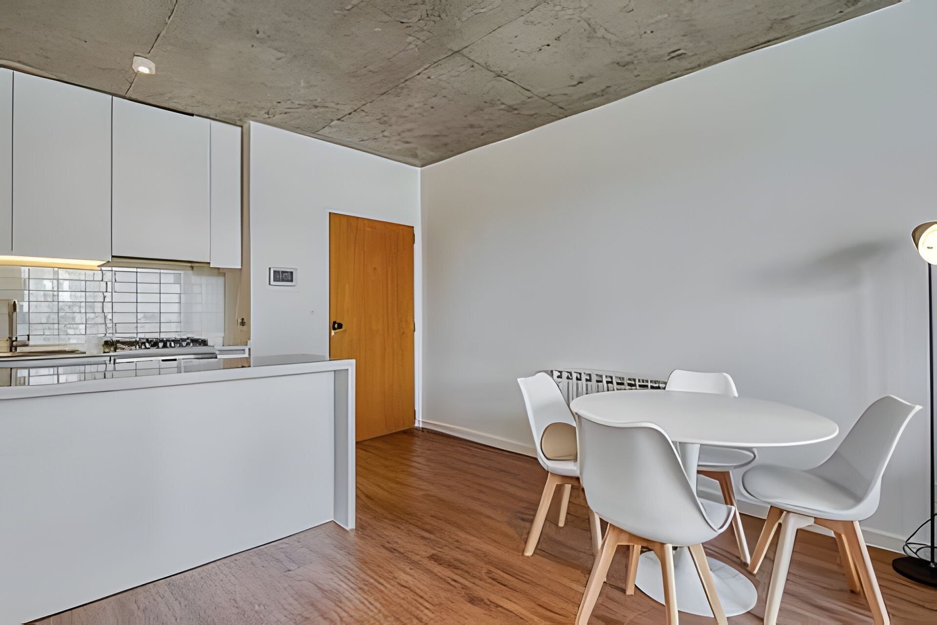 A modern kitchen with white cabinets, a wooden door, and a dining area with a round table and four chairs.