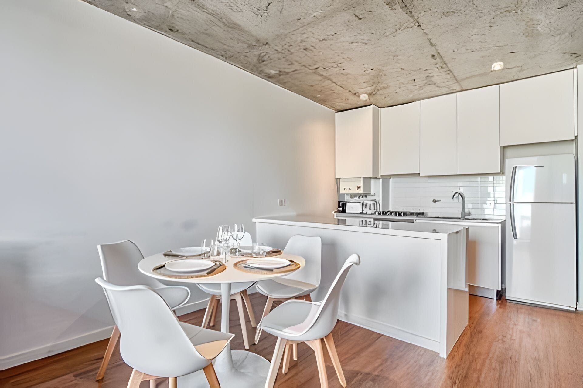 Una cocina moderna con armarios blancos, una isla central y un comedor con sillas blancas.