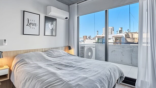 Een moderne slaapkamer met een groot bed, stadszicht door een raam en een plafondventilator.