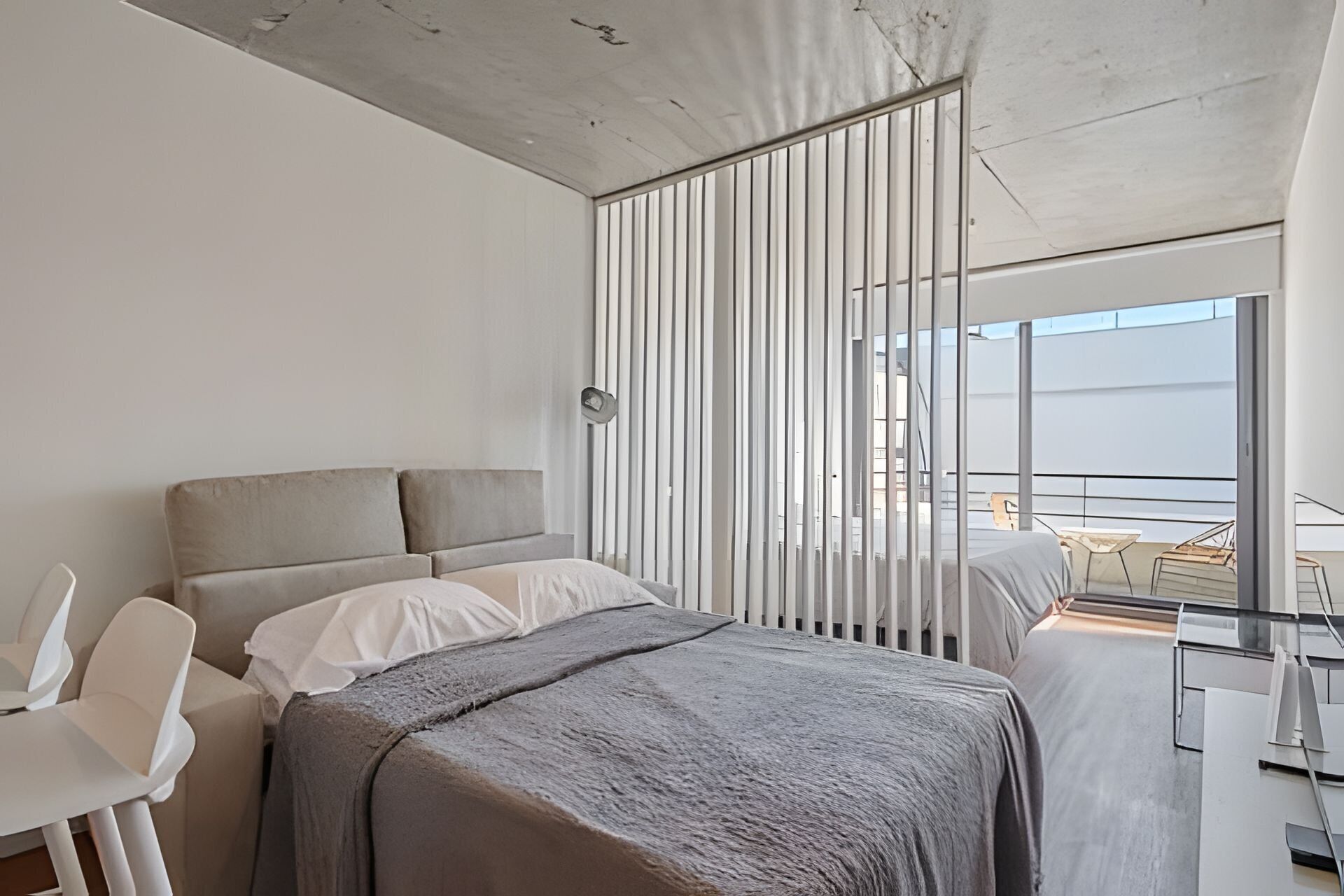A modern hotel room with a large bed, a desk, and a view of the balcony.