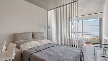 A modern hotel room with a large bed, a desk, and a view of the balcony.