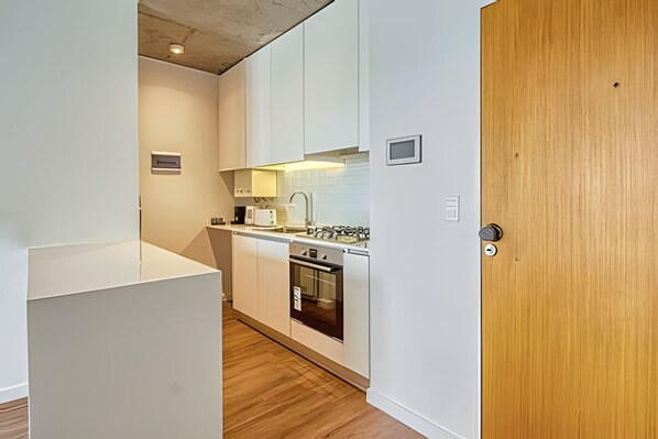 Una cocina compacta con armarios blancos, horno integrado y microondas.