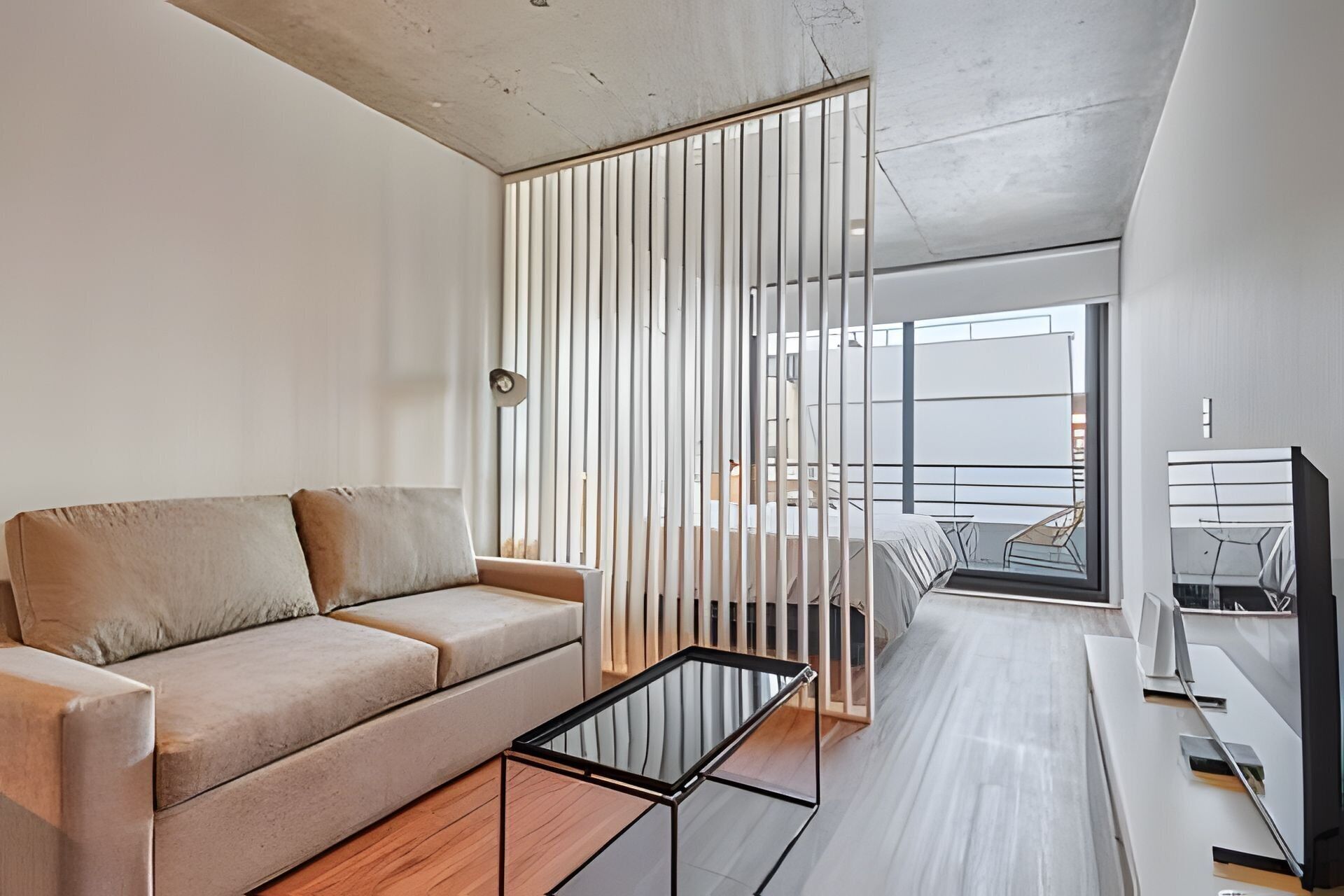 A modern living room with a sofa, a coffee table, and a view through a window with vertical blinds.