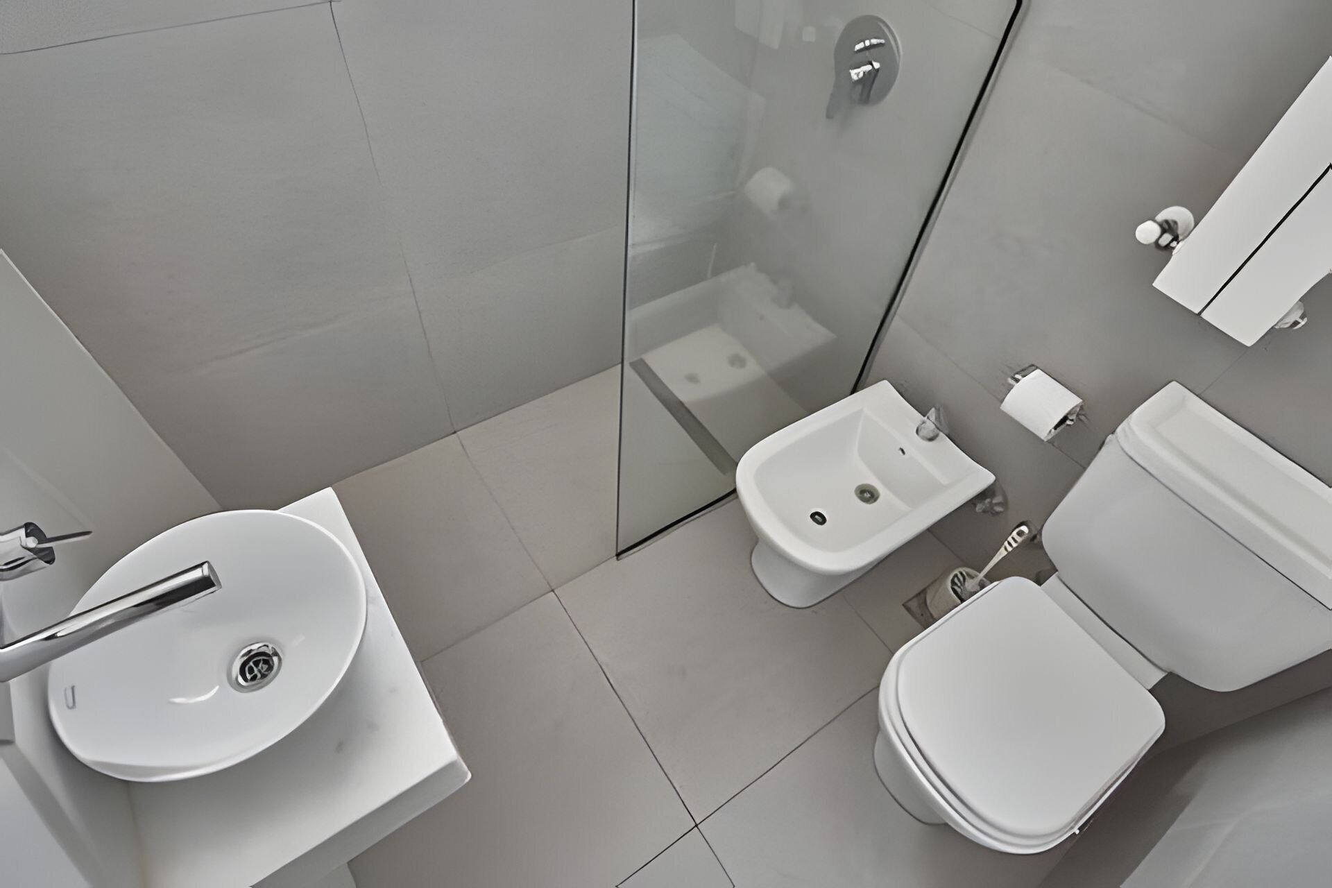 A modern bathroom with a sink, bidet, toilet, and glass shower enclosure.