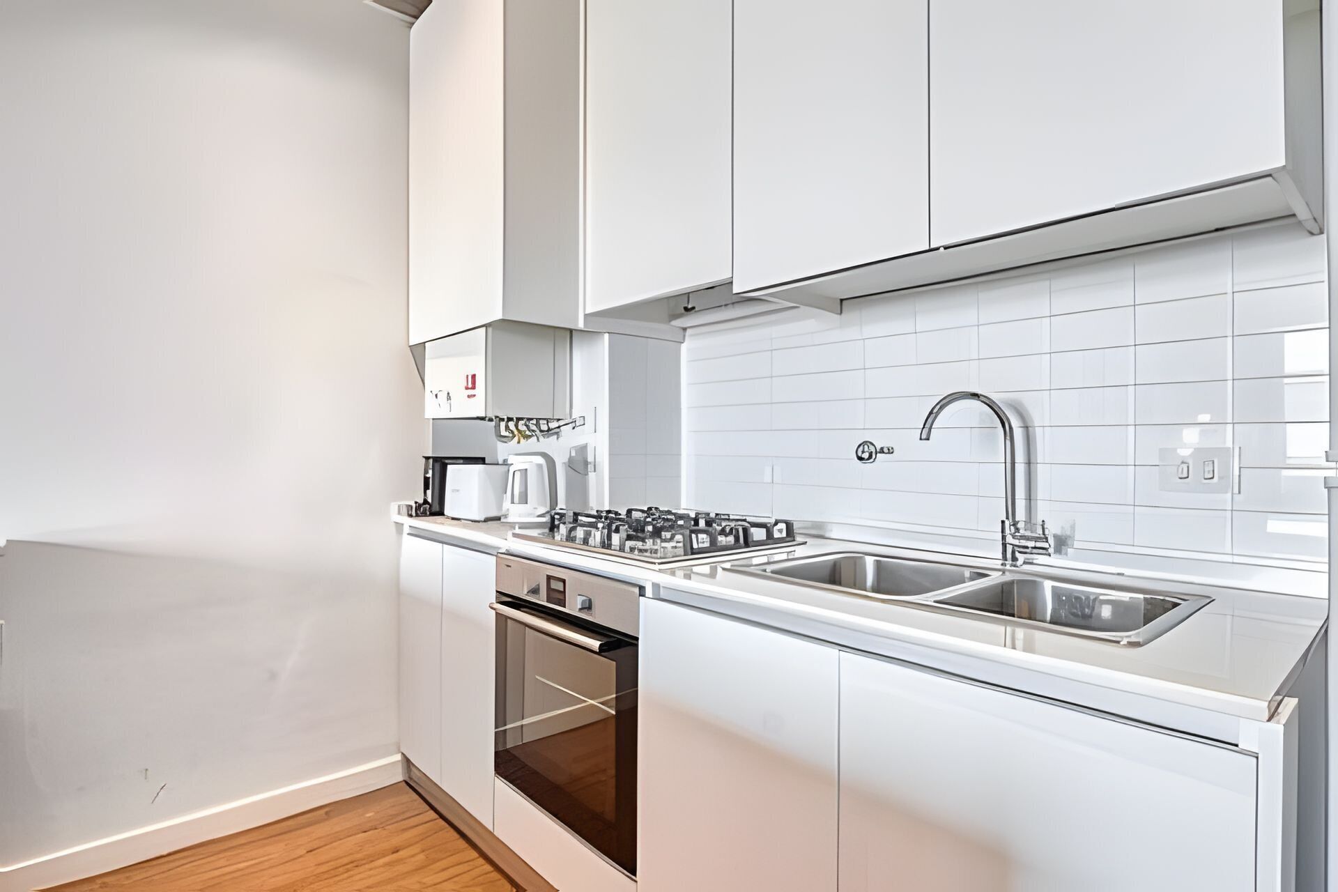 A modern kitchen with white cabinets, a stainless steel sink, and a built-in oven.