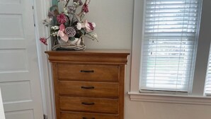 A wooden dresser with four drawers and a vase of flowers on top, positioned in a room with a window and a door. - Relax Inn The Grove (Forest Grove)