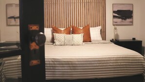 Ein ordentlich bezogenes Bett mit gestreifter Bettwäsche und dekorativen Kissen, ein Nachttisch mit Lampe sowie zwei gerahmte Bilder an der Wand.