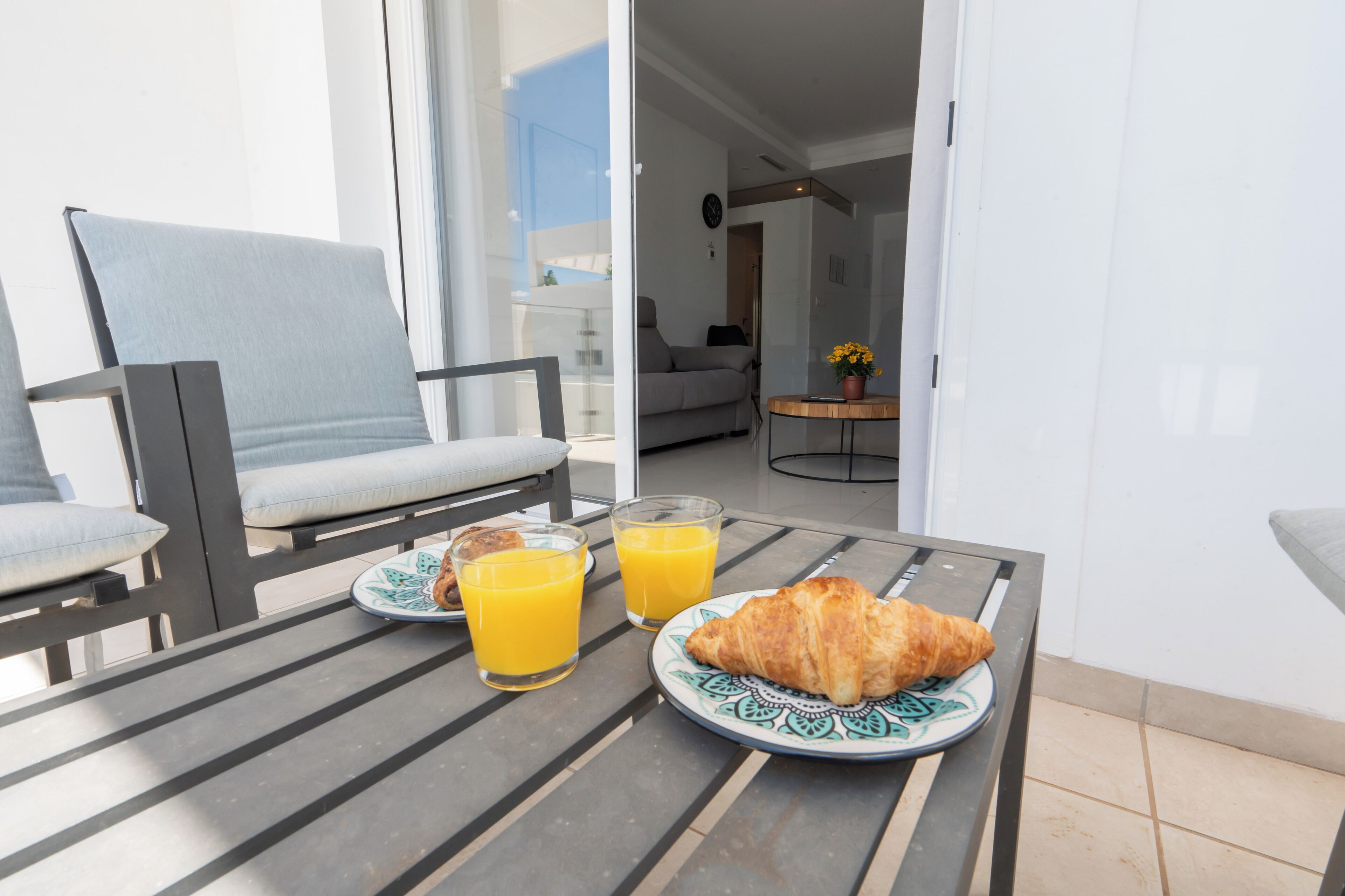 Un balcón con una mesa dispuesta para el desayuno, incluyendo cruasanes y zumo de naranja.