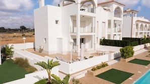 A modern white building with multiple balconies, a swimming pool, and a landscaped garden.