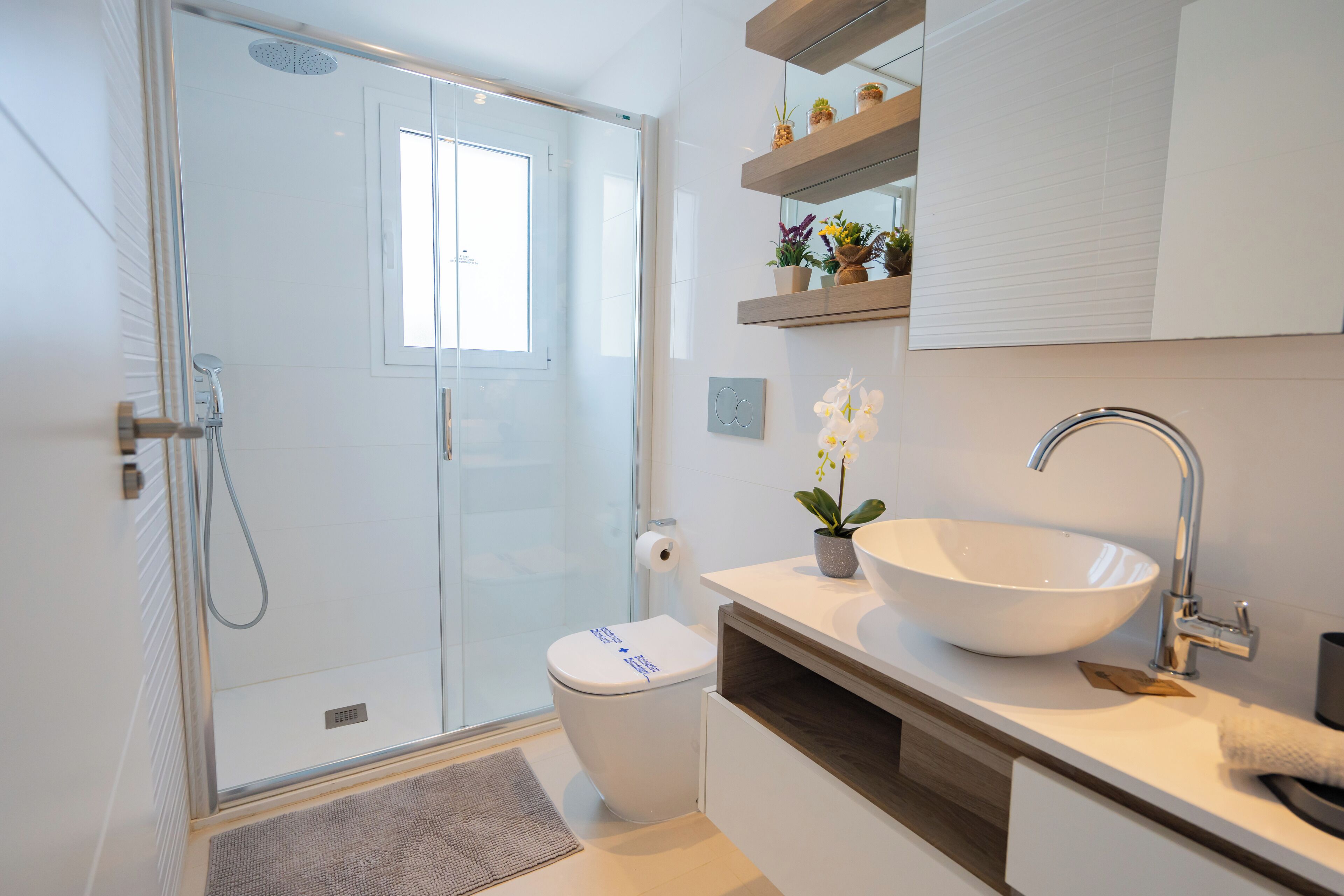 Un bagno moderno con box doccia in vetro, un water bianco, un ampio lavandino bianco e un mobile bagno in legno.