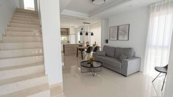 Una sala de estar moderna con una escalera, un sofá gris, una mesa de centro y un comedor con una cocina al fondo.