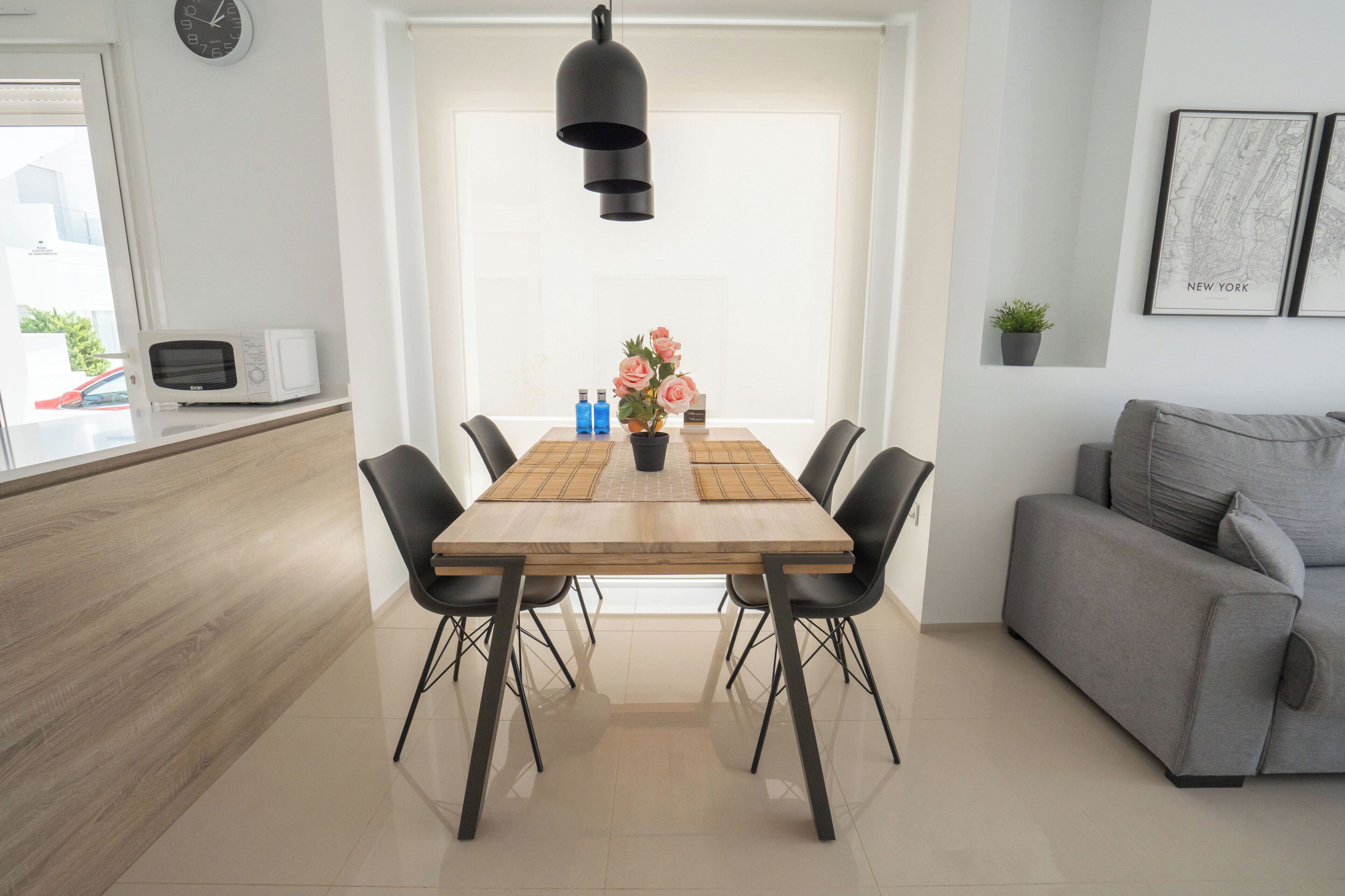 Un comedor moderno con una mesa de madera, sillas negras, una lámpara colgante negra y una planta en maceta.