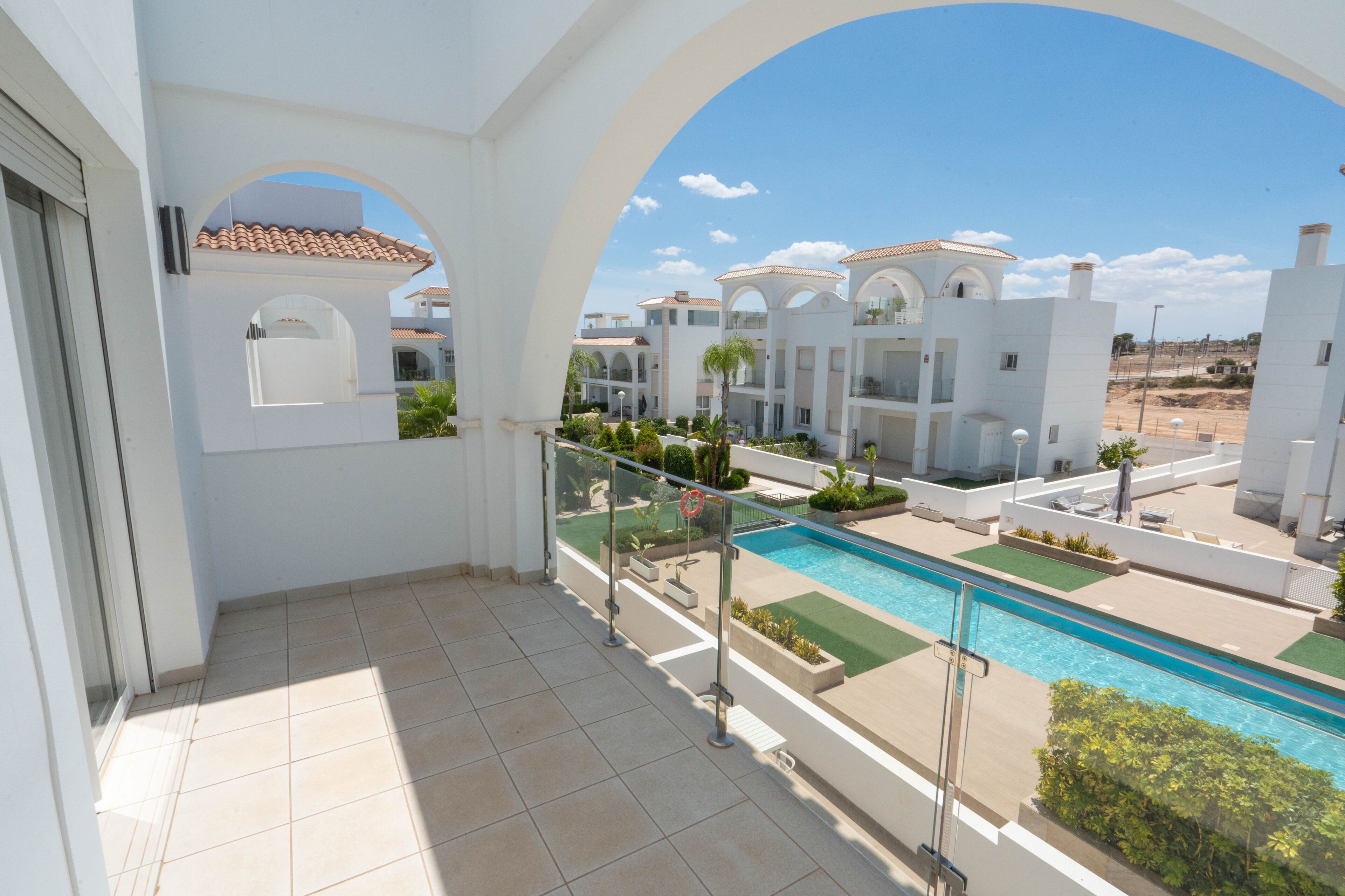 A balcony with a view of a swimming pool, white buildings, and a clear sky.