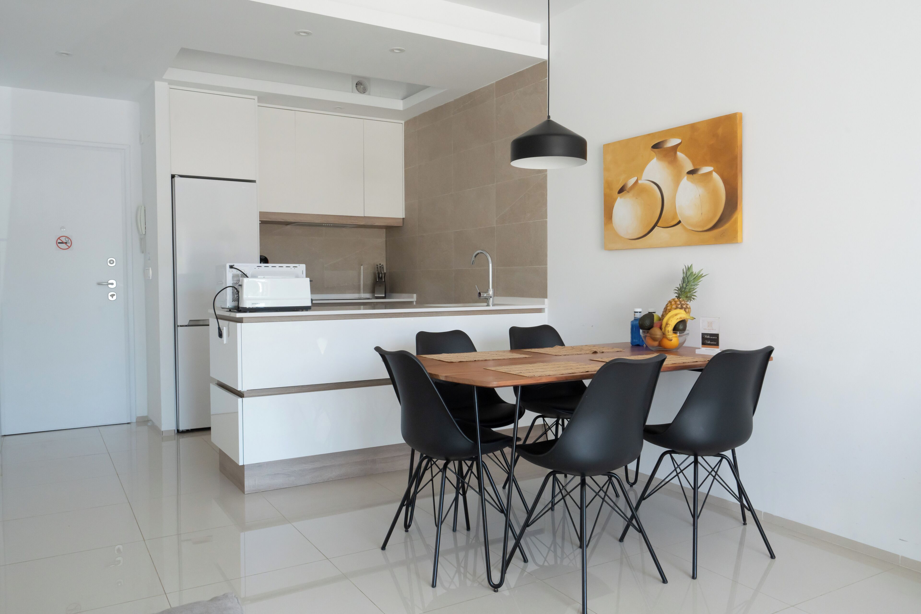 A modern kitchen with white cabinets, a built-in oven, and a dining area with a wooden table and black chairs.
