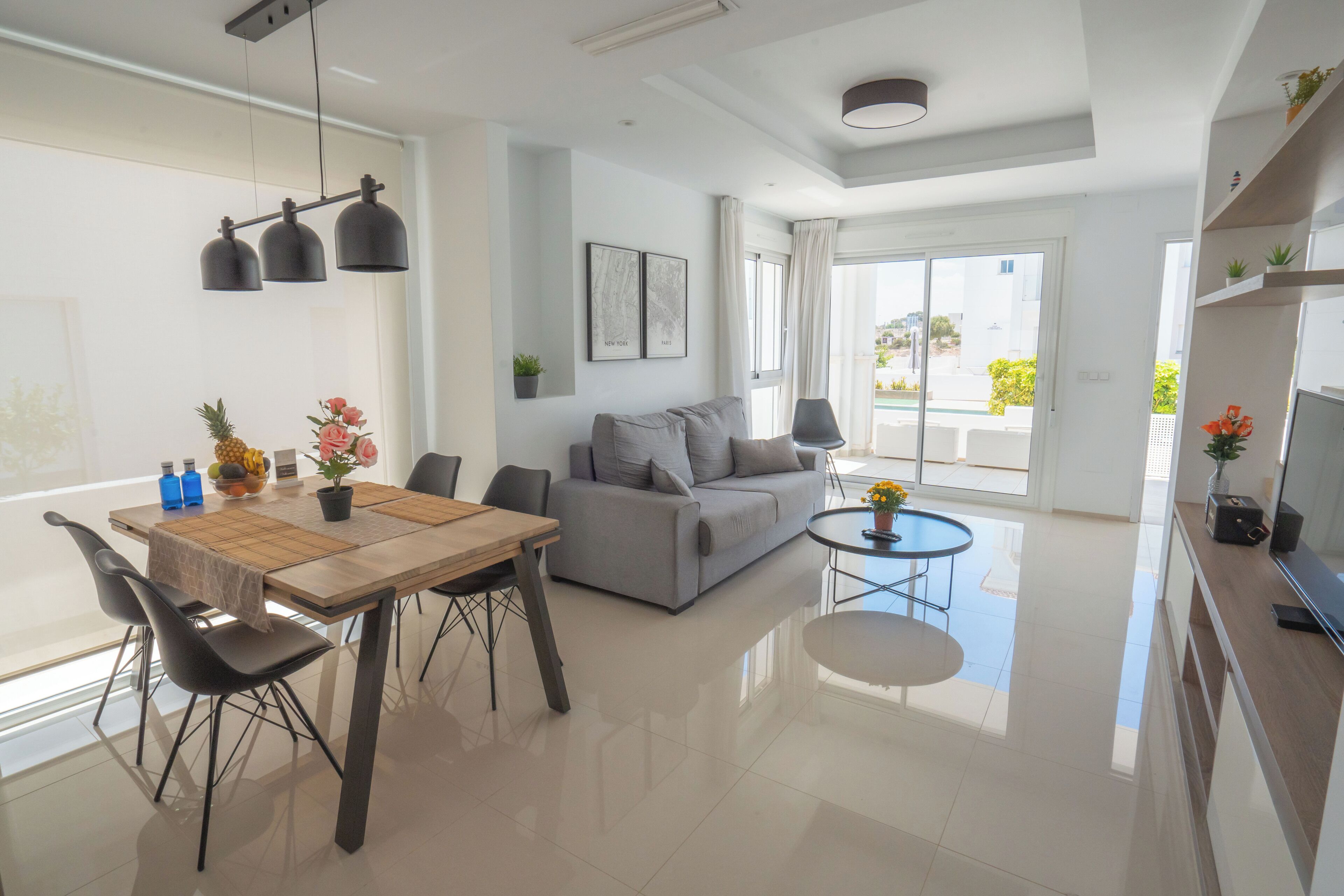 A modern living room with a dining area, a grey sofa, a round coffee table, and a TV on a wooden cabinet.