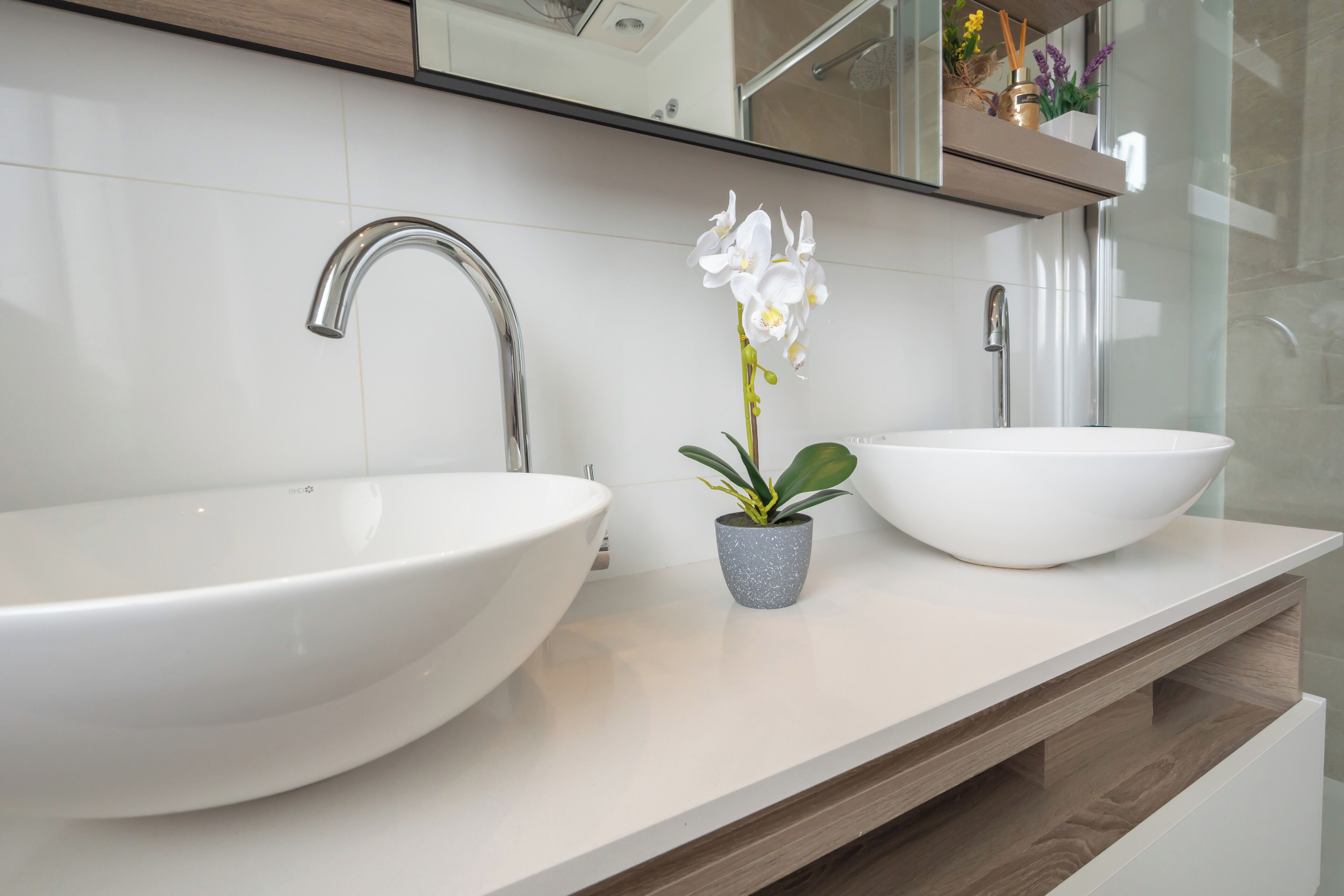 A modern bathroom with two large white sinks, a single faucet, and a small potted orchid on the countertop.