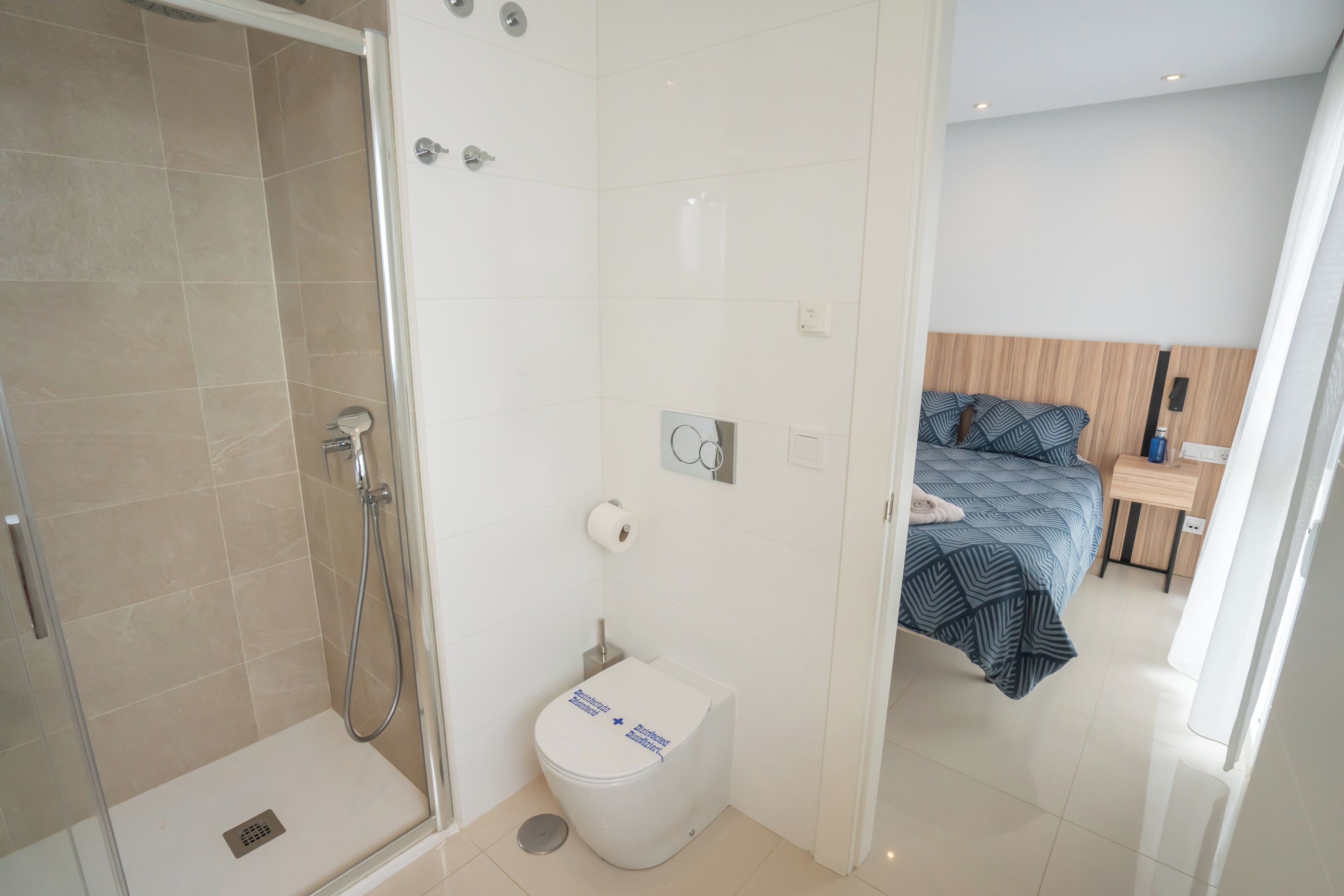 A modern bathroom with a shower, toilet, and a bed in the adjacent room.