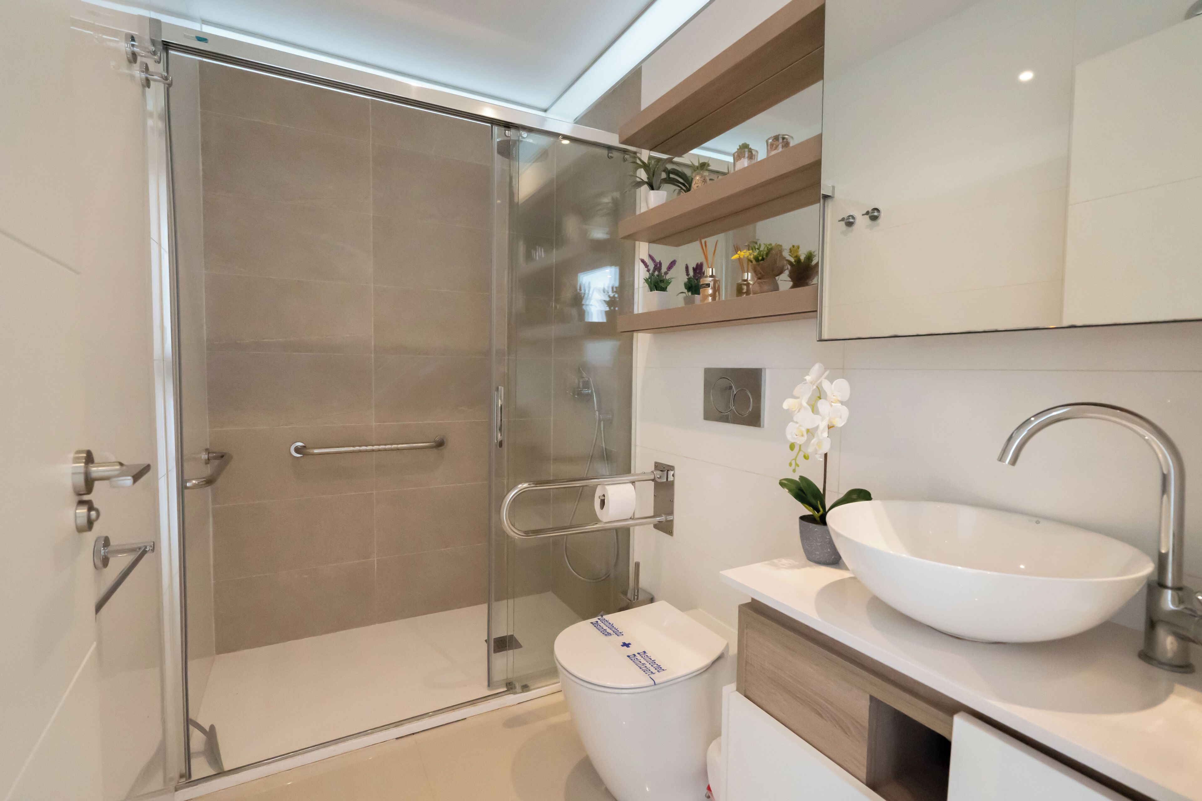 A modern bathroom with a glass-enclosed shower, a white sink, and a wooden vanity.