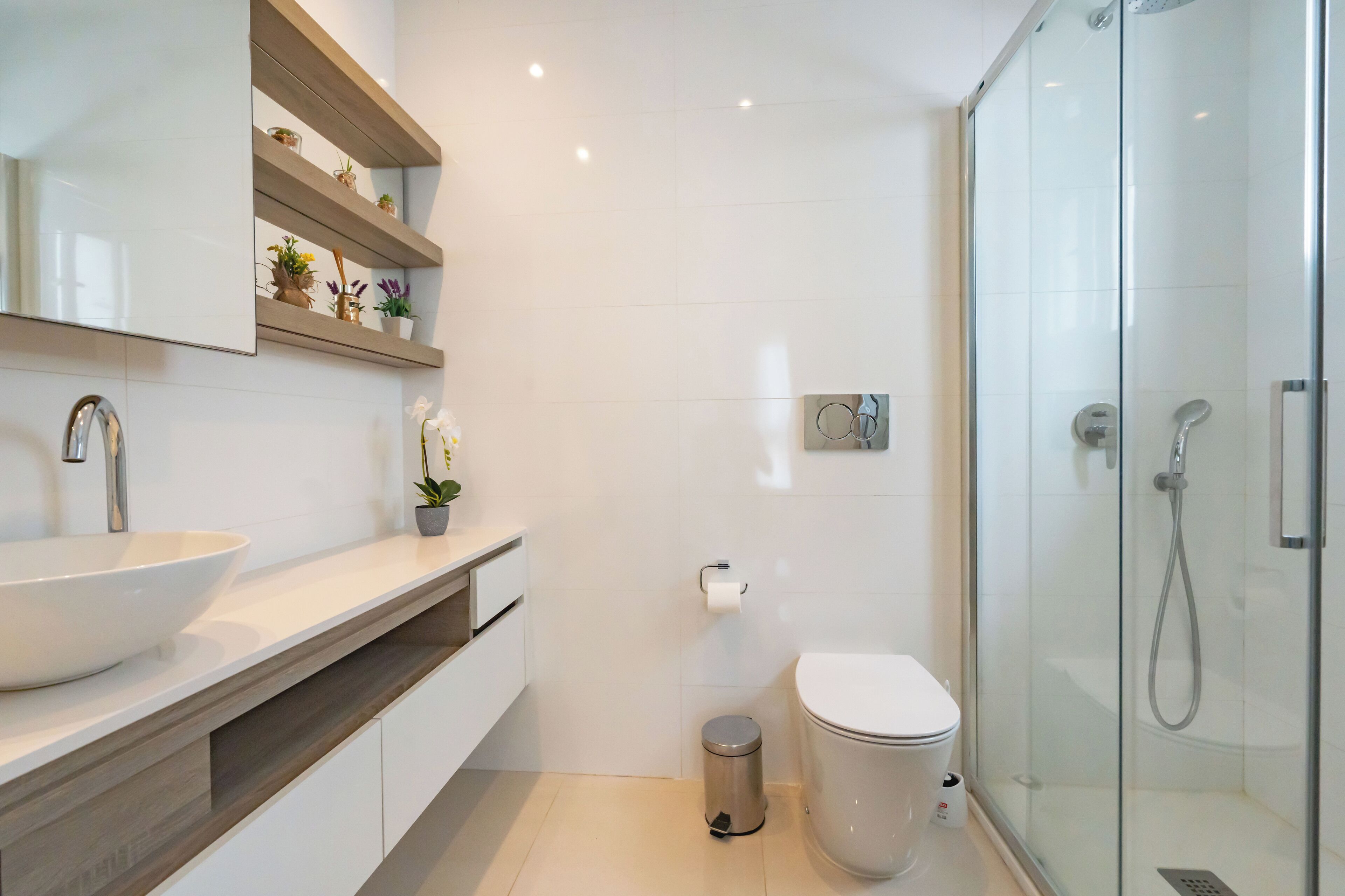 A modern bathroom with a large white sink, a toilet, a glass shower enclosure, and a mirror with shelves above.