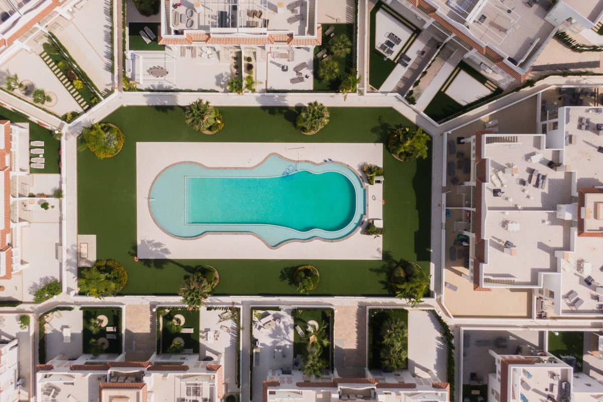 An aerial view of a residential complex with a central swimming pool, surrounded by well-maintained lawns and a variety of house layouts.