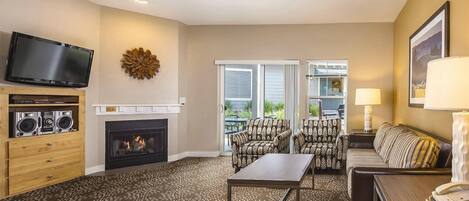 A living room with a fireplace, a television, patterned furniture, and a view through the glass doors.