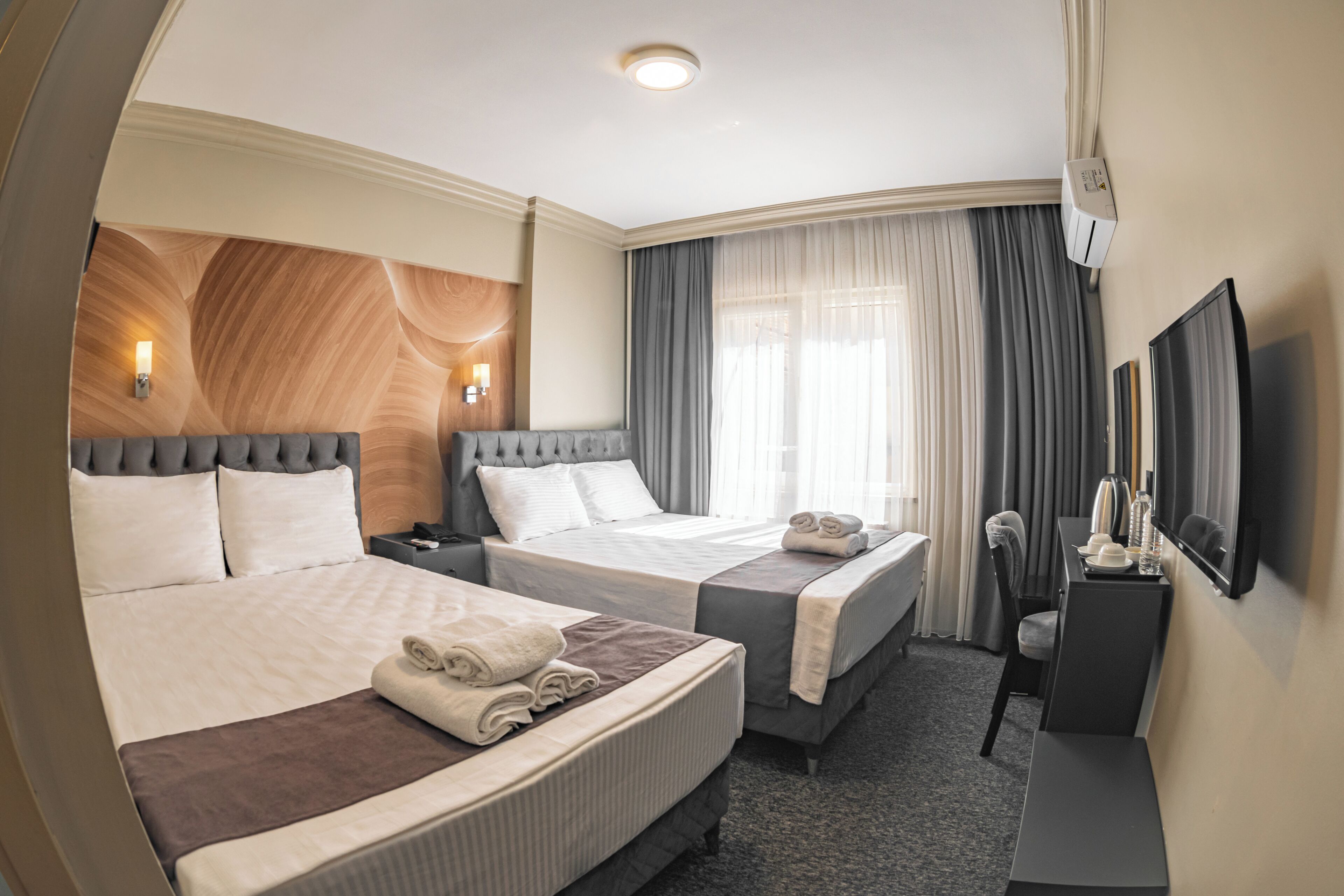 Quarto de hotel com duas camas, uma escrivaninha, uma cadeira, uma televisão e uma janela com cortinas.