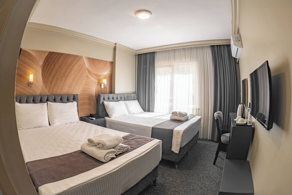 Een hotelkamer met twee bedden, een bureau, een stoel, een televisie en een raam met gordijnen.