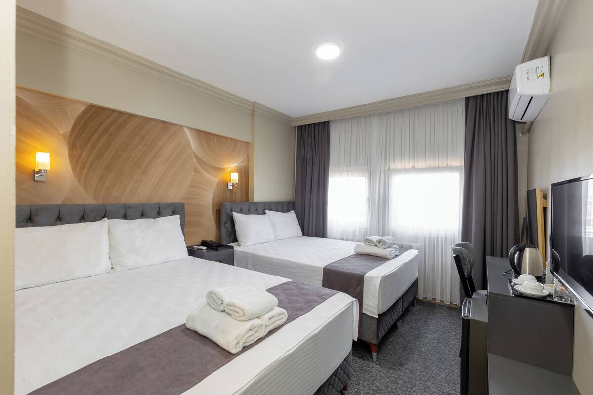 Een hotelkamer met twee bedden, een bureau, een stoel, een televisie, een airconditioner en een raam met gordijnen.