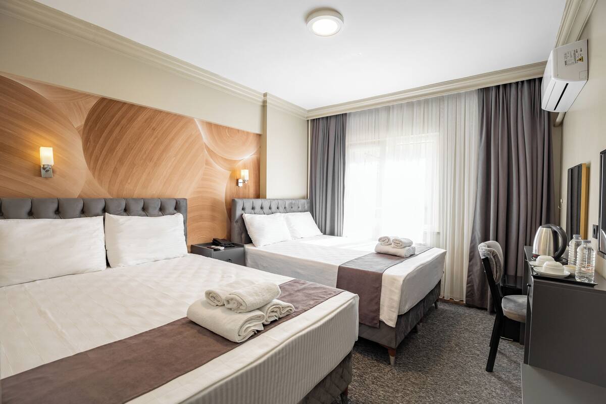 Quarto de hotel com duas camas, uma escrivaninha, uma cadeira e um minibar.