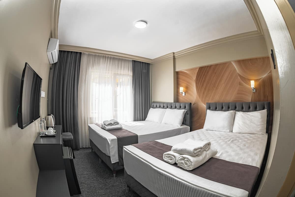 Een hotelkamer met twee bedden, een bureau, een flatscreen-tv en een raam met gordijnen.