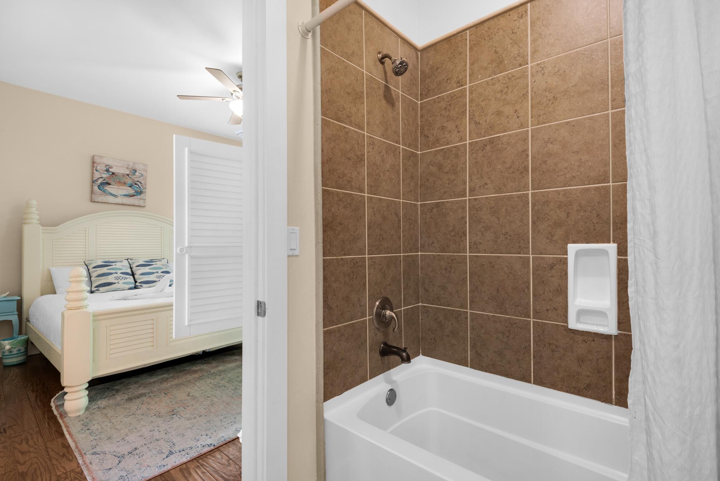 A bedroom with a bed, a nightstand, a ceiling fan, and a bathroom with a bathtub and shower.