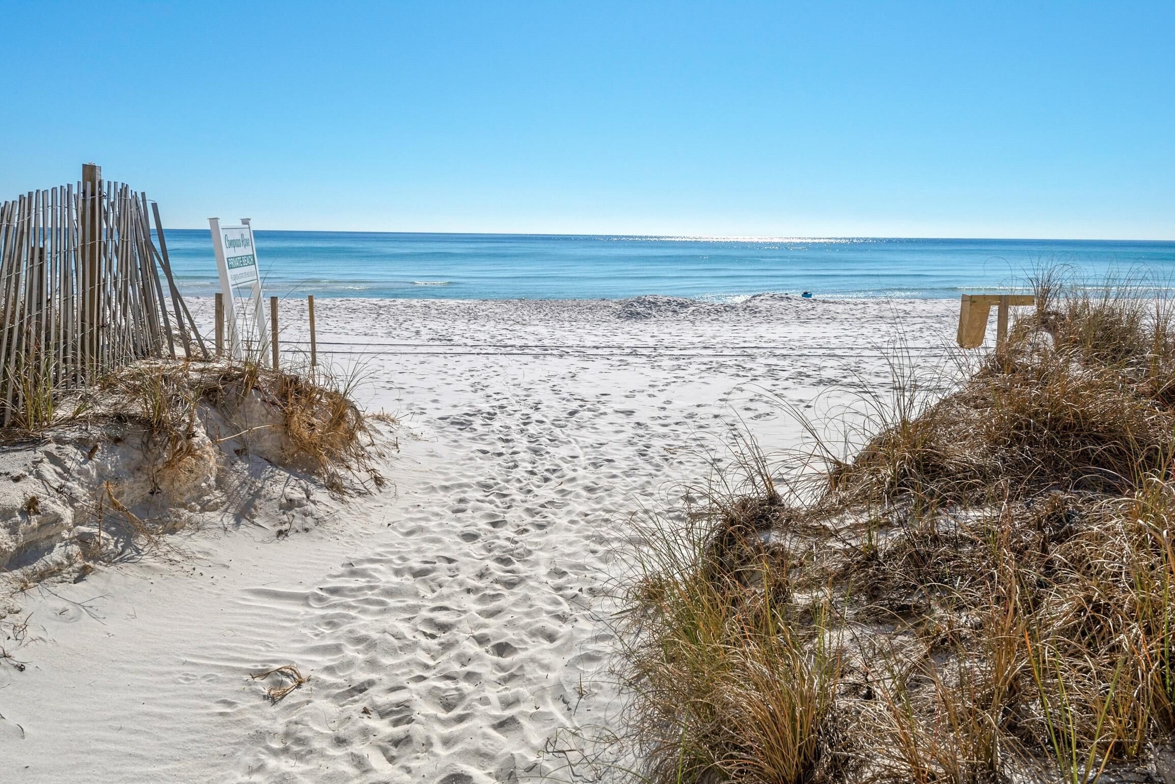 A sandy beach with a wooden fence and a sign.