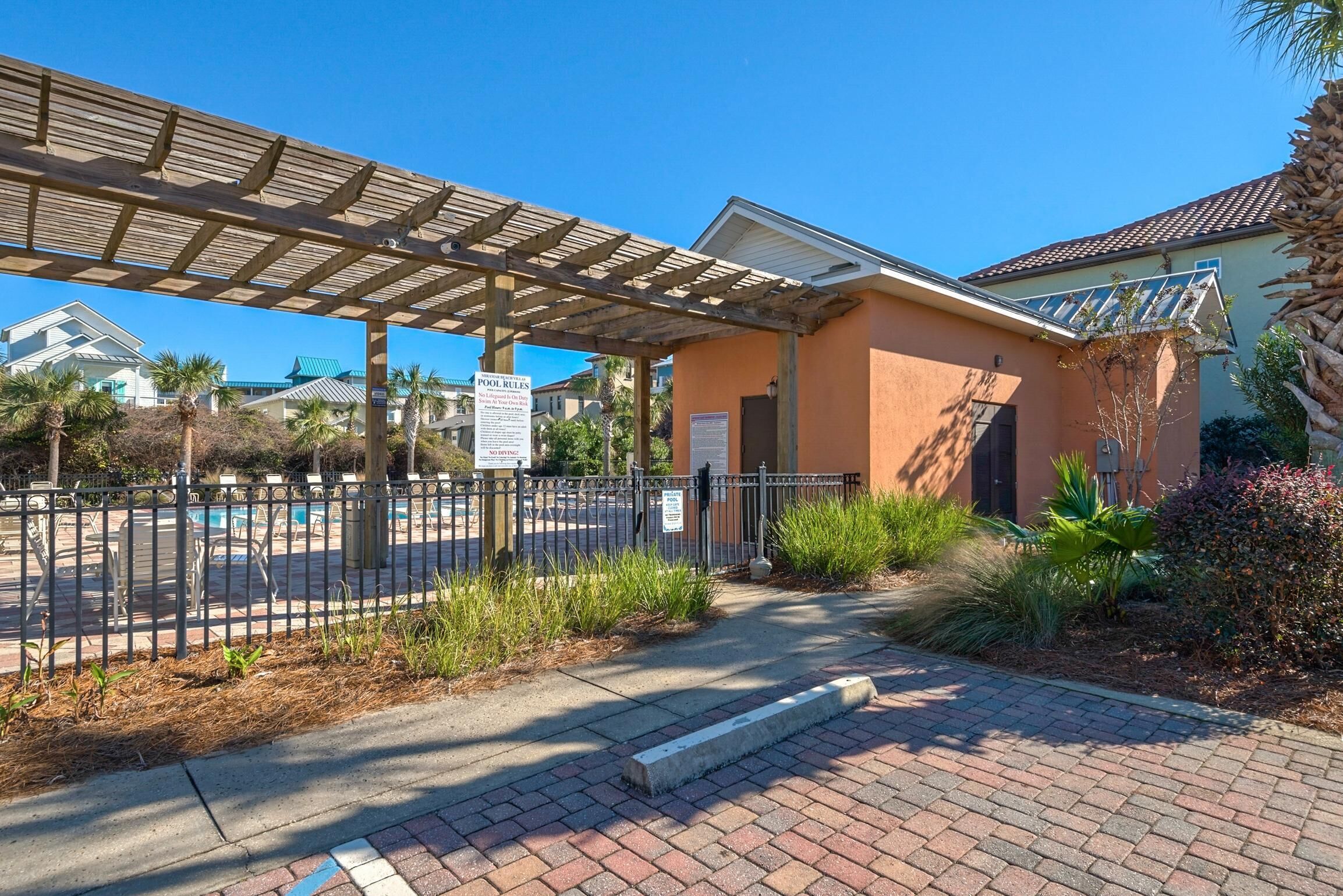 A covered outdoor area with a pool, surrounded by a fence and palm trees.