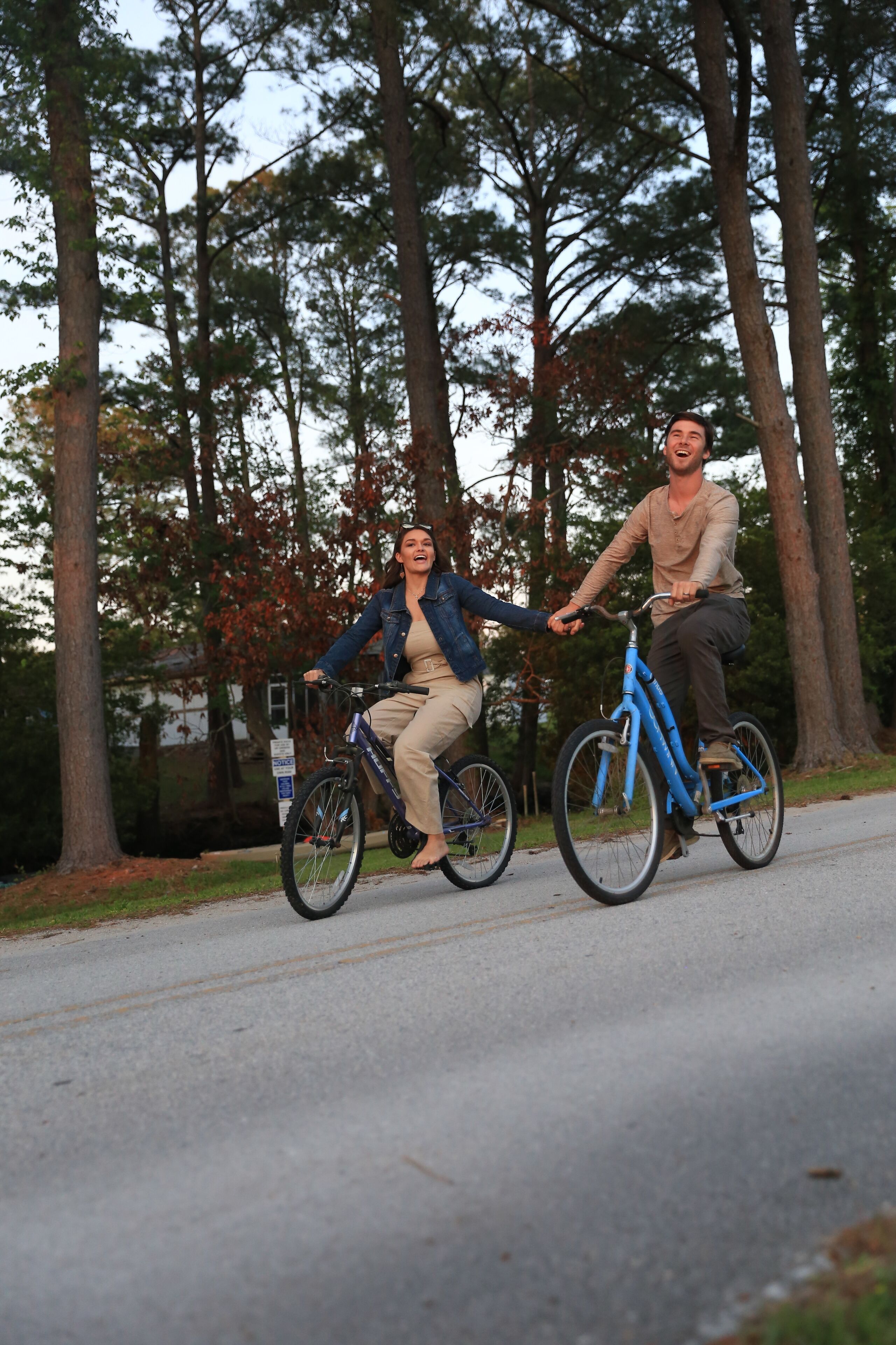 Deux personnes font du vélo sur un chemin pavé, bordé de grands arbres.