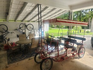 Un garaje techado con bicicletas, un triciclo rojo y una mesa con sillas.