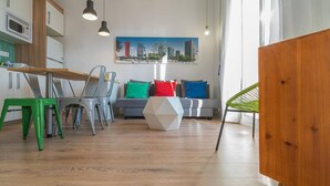 Una cocina moderna con comedor, un sofá gris con cojines de colores y un cuadro de paisaje urbano en la pared.
