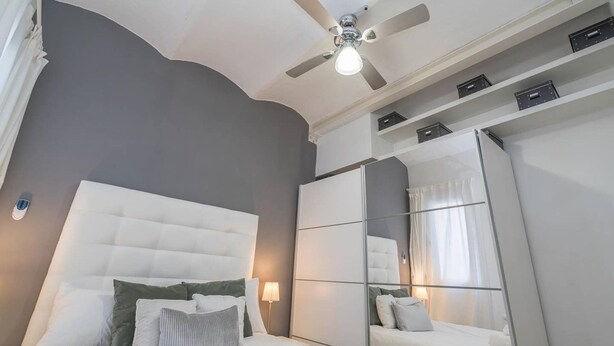 Una habitación de hotel moderna con una cama grande, un ventilador de techo, un espejo y estantes empotrados.