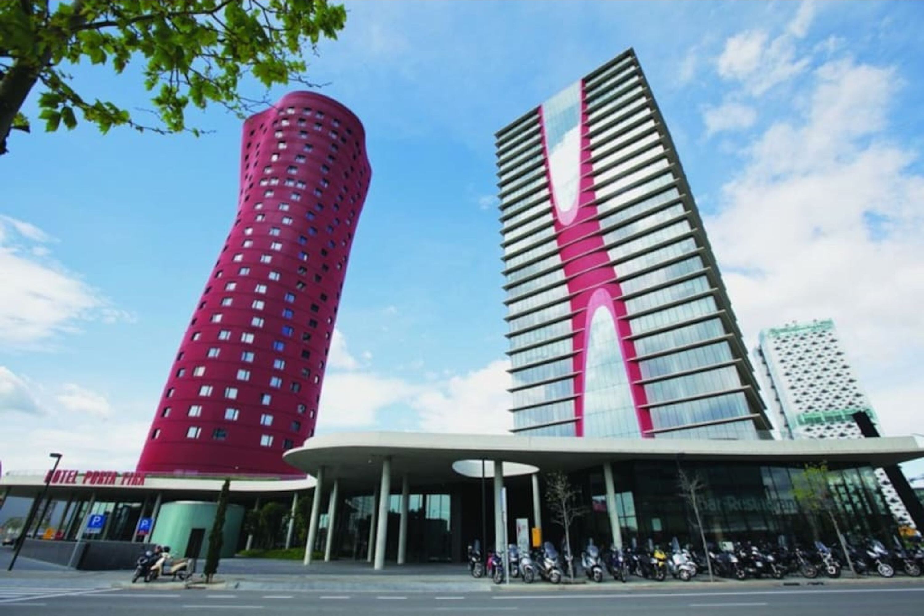 Ett modernt hotell med en distinkt, röd, cylindrisk byggnad och en hög, vit och rosa struktur.