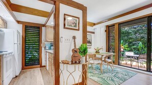 Una cocina con vigas de madera, una zona de comedor con una mesa y sillas, y vistas a la vegetación exterior.