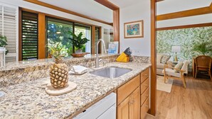 Una cocina con encimeras de granito, pileta de acero inoxidable, armarios de madera y un comedor con una silla y una mesa.