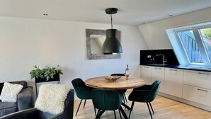 A modern kitchen with a dining area, featuring a round wooden table, green chairs, and a black pendant light. - Modern apartment, bright and comfortable with private terrace (Limmen)
