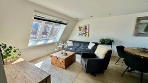 A modern living room with a sofa, coffee table, and dining area. - Modern apartment, bright and comfortable with private terrace (Limmen)