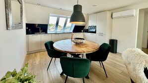 A modern kitchen with white cabinets, a round wooden table, and green chairs. - Modern apartment, bright and comfortable with private terrace (Limmen)