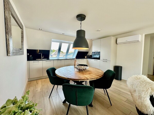 Una cocina moderna con armarios blancos, una mesa redonda de madera y sillas verdes.