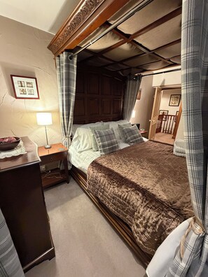 A bedroom with a four-poster bed, a bedside table with a lamp, and a dresser.