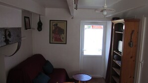Une pièce avec un canapé rouge, une petite table ronde, un meuble en bois et une porte donnant sur l’extérieur.