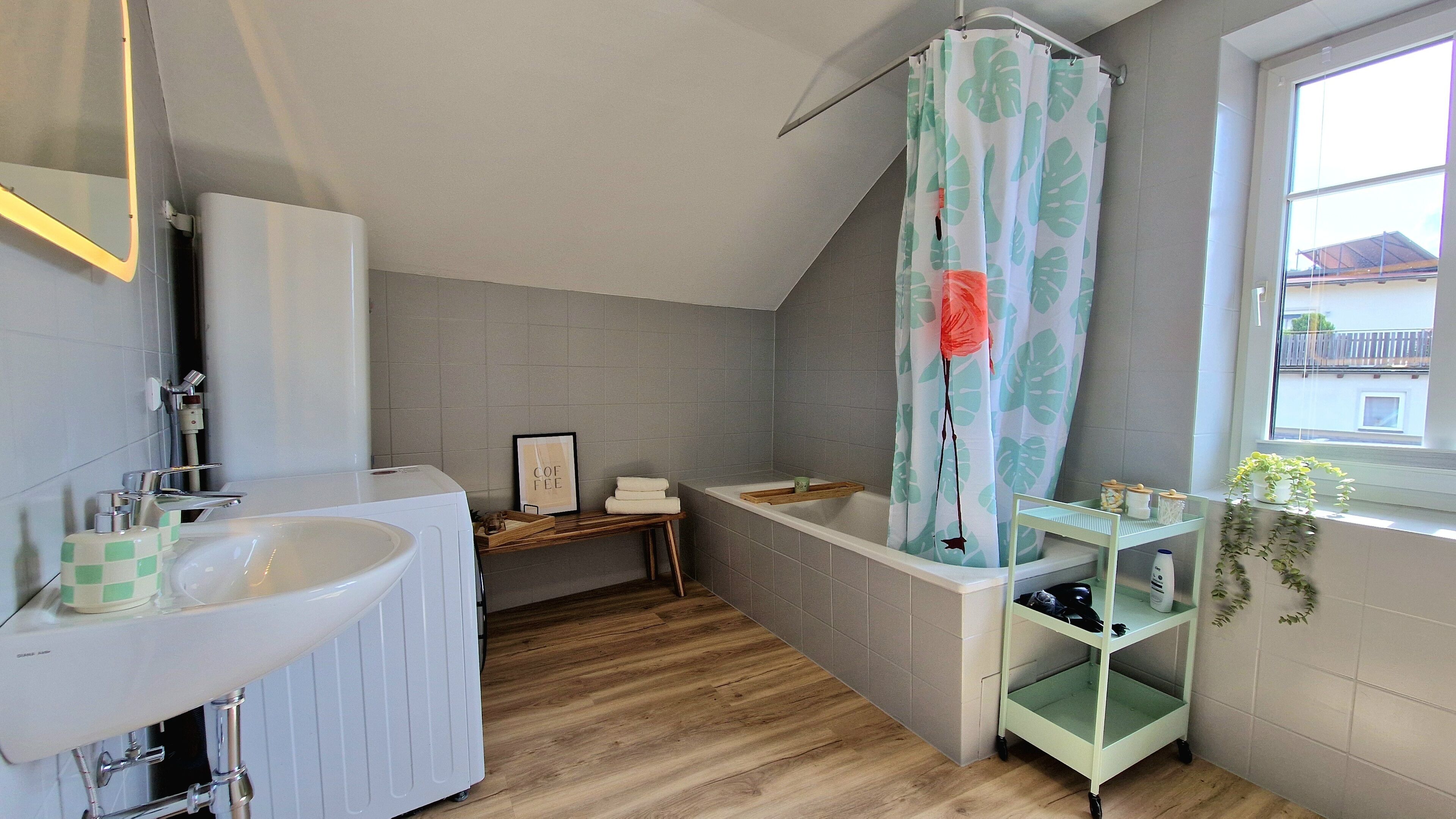 Ein Badezimmer mit Badewanne, Waschbecken, Spiegel und einer Duschvorhang mit Blättermotiv.