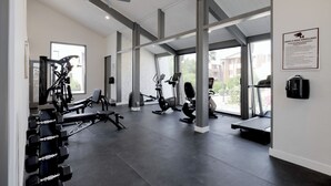 A gym with various exercise equipment, large windows, and a ceiling fan.