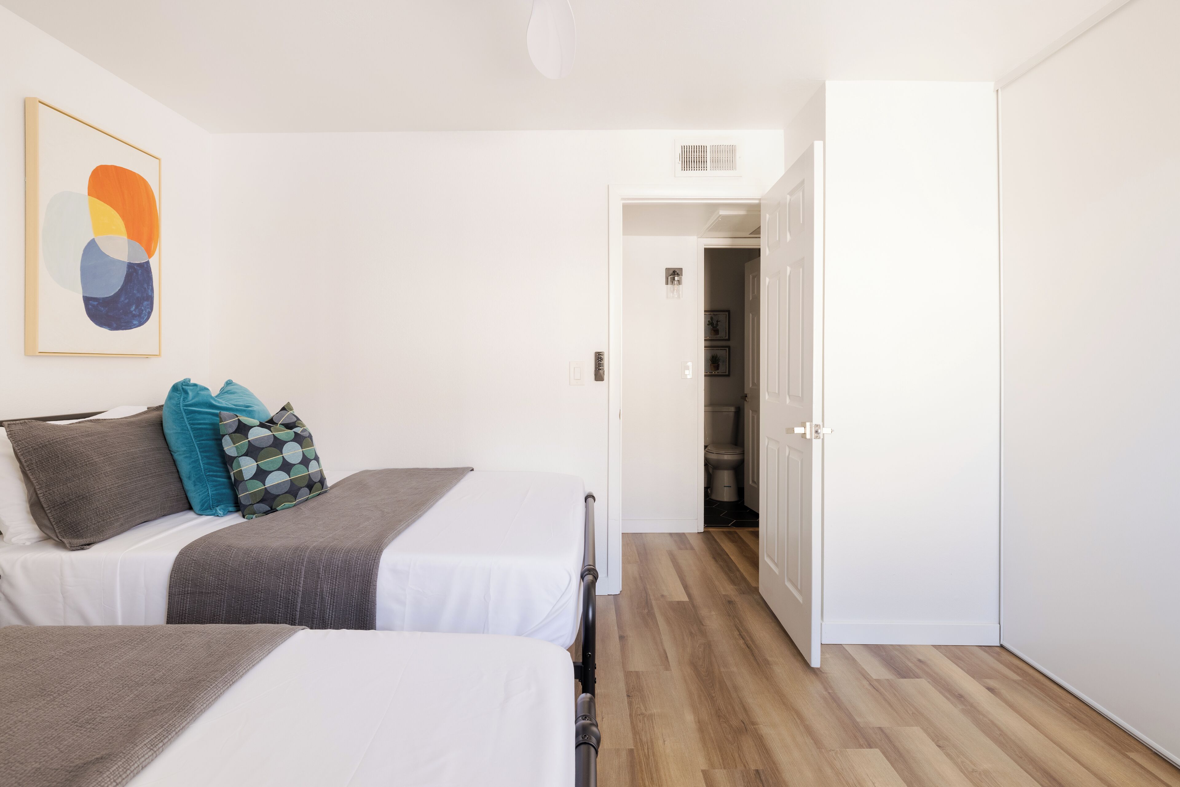 A hotel room with two beds, a wardrobe, and a hallway leading to a bathroom.