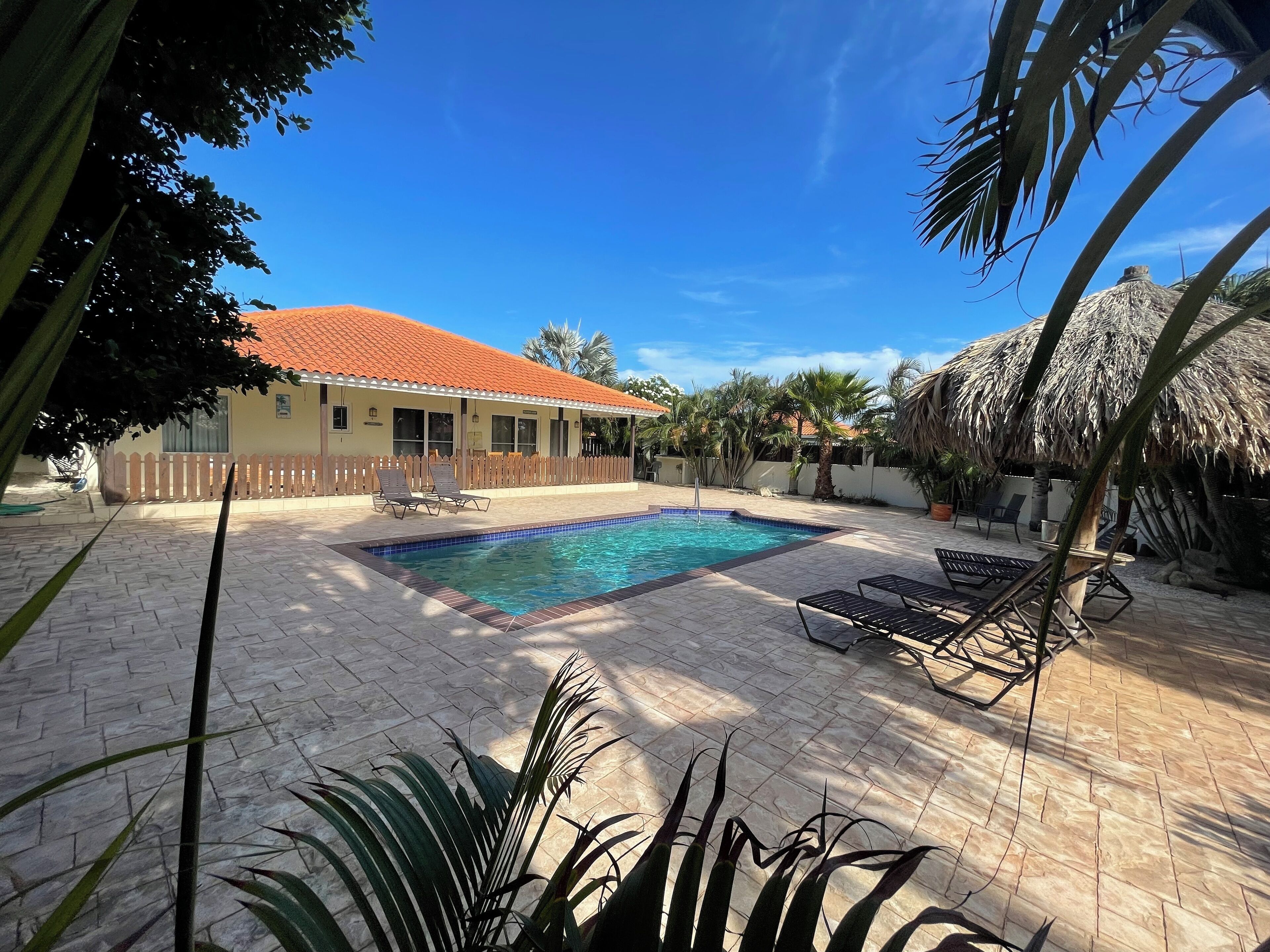 A swimming pool with lounge chairs, a fenced area, and a building with a red roof.